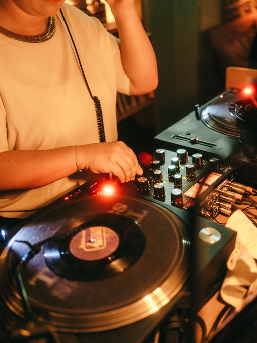 Close up of a DJ playing music inside the Shoreditch-based Seed Library hotel bar at a night party with warm lights.